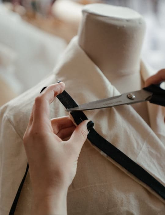 Manos con tijeras cortando el ribete de un saco sobre un maniquí