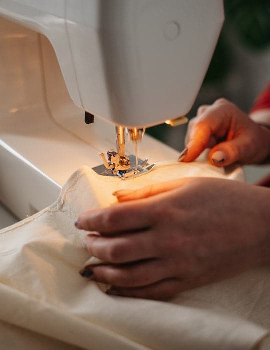 Primer plano de una máquina de coser iluminada mientras unas manos guían la tela