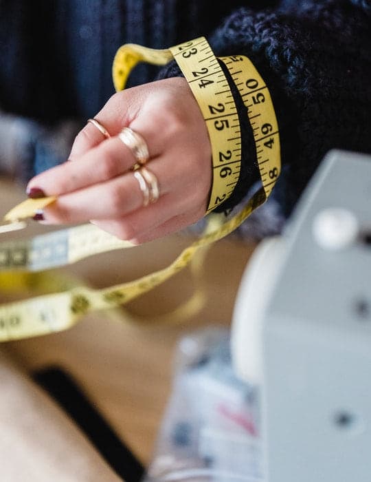 Manos con una cinta métrica amarilla sobre la muñeca, tomando medidas